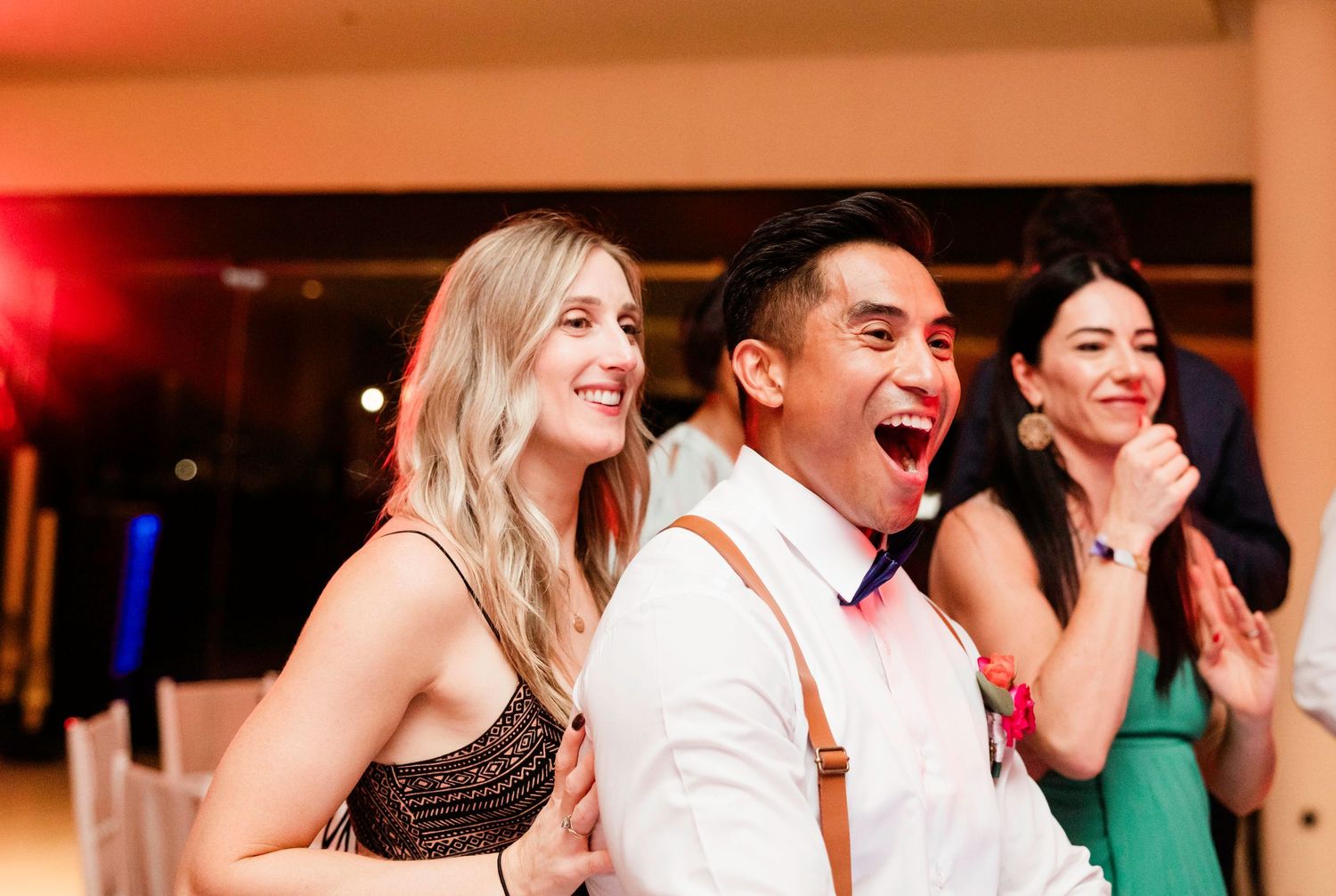A group of people in formal attire laugh together at a celebratory event with warm lighting.