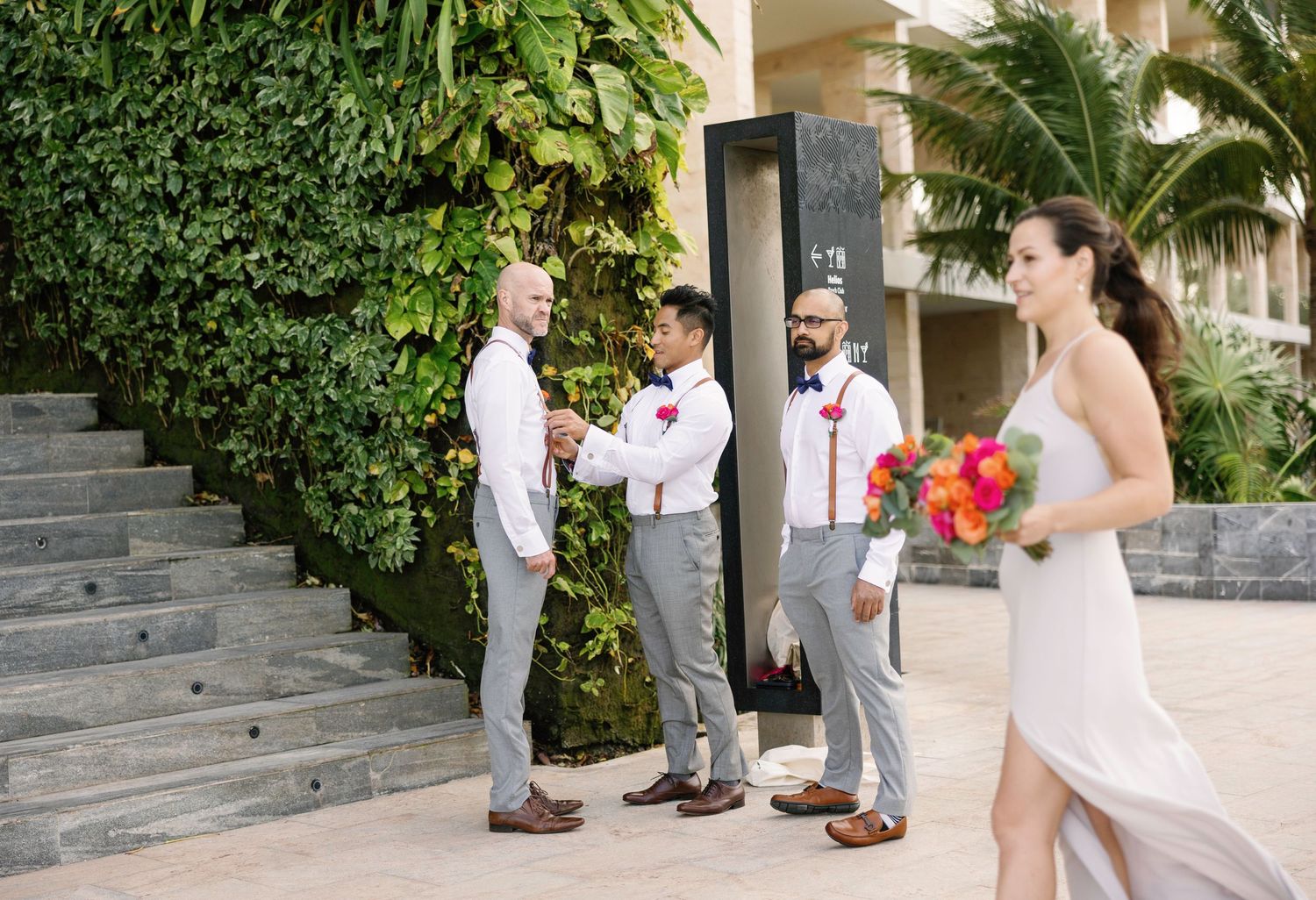 Wedding party members walk along stone steps surrounded by lush tropical greenery.