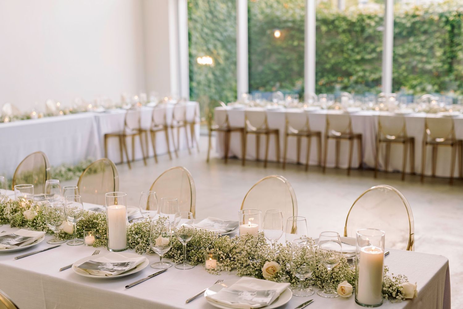 Elegant wedding reception tables set with gold accents and white linens in a bright venue.
