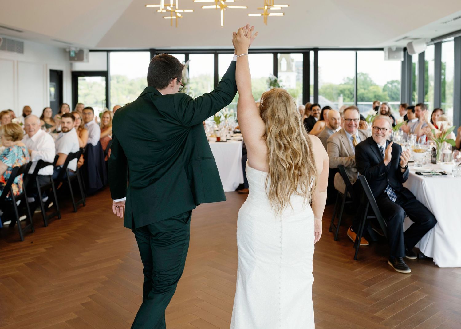 Wedding reception dance floor with guests dancing under modern chandeliers.