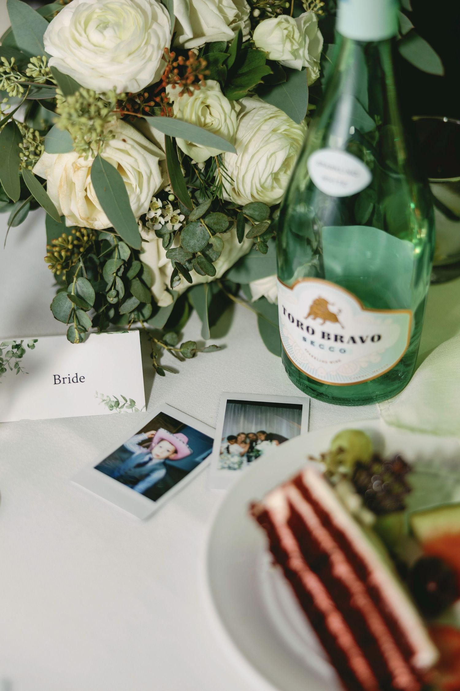 White roses and greenery arrangements alongside place cards on an elegant table setting.