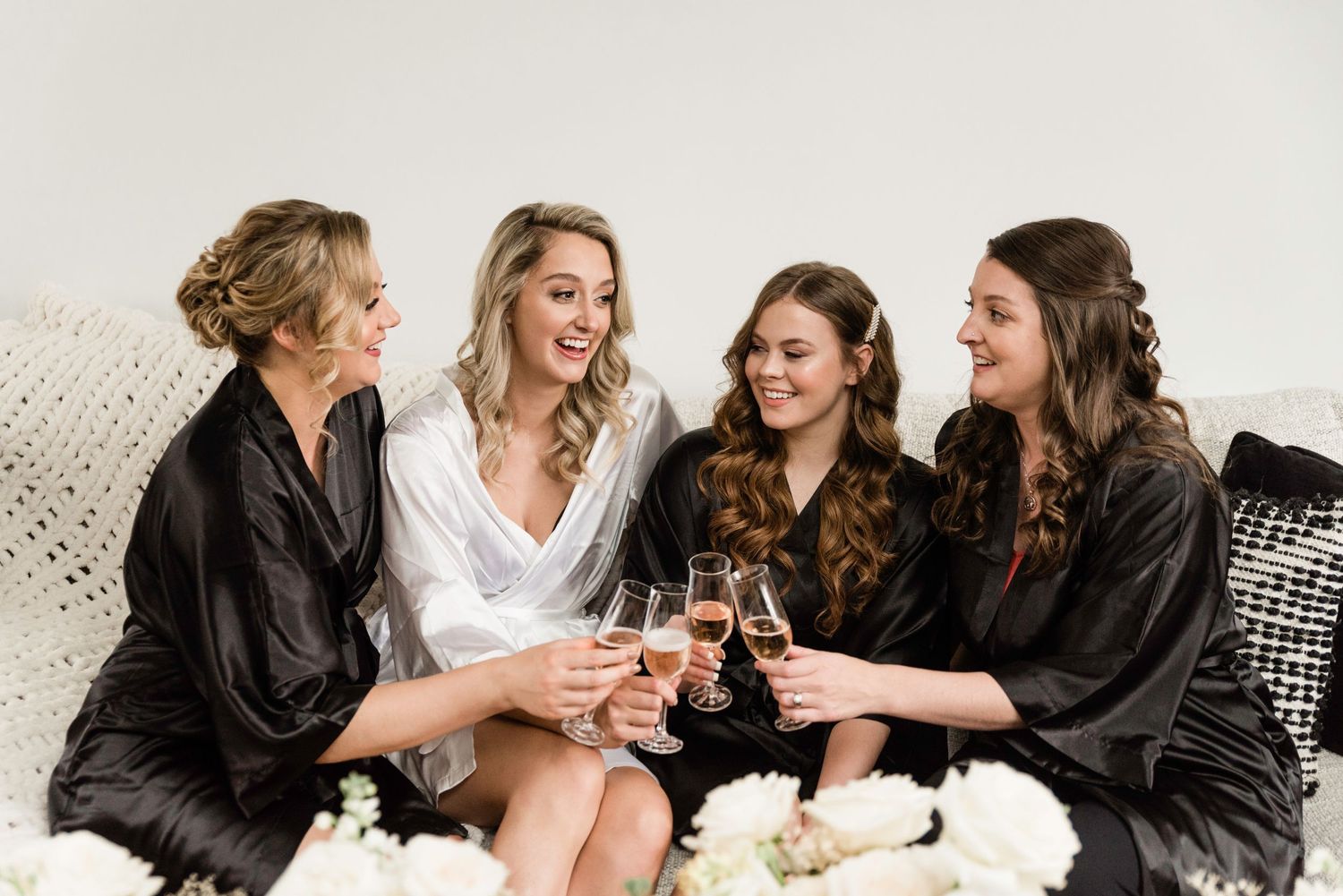 Wedding party toasts and celebrates with champagne while wearing black robes and white dresses.