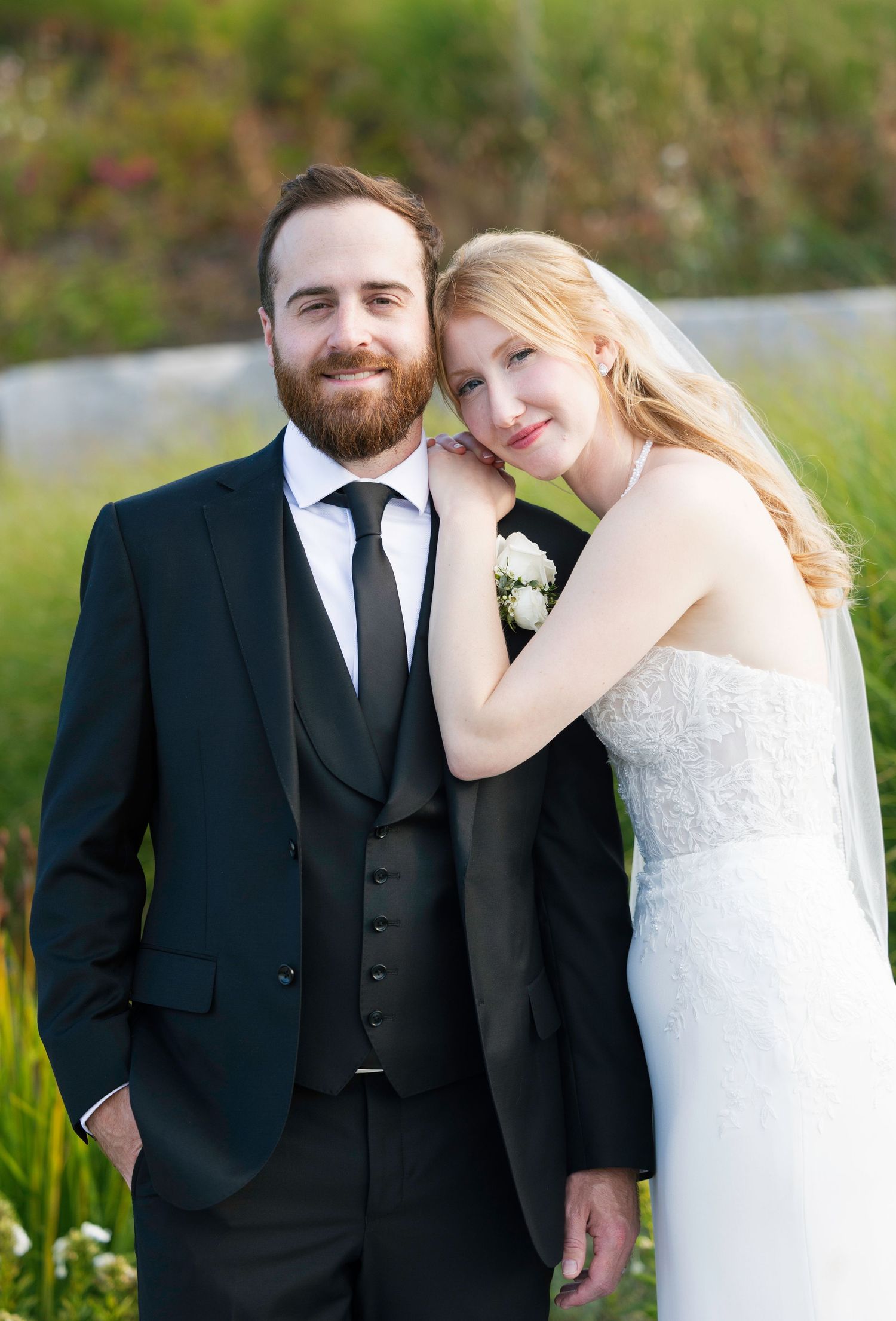 A bride and groom pose together in a romantic outdoor setting with green foliage in the background.