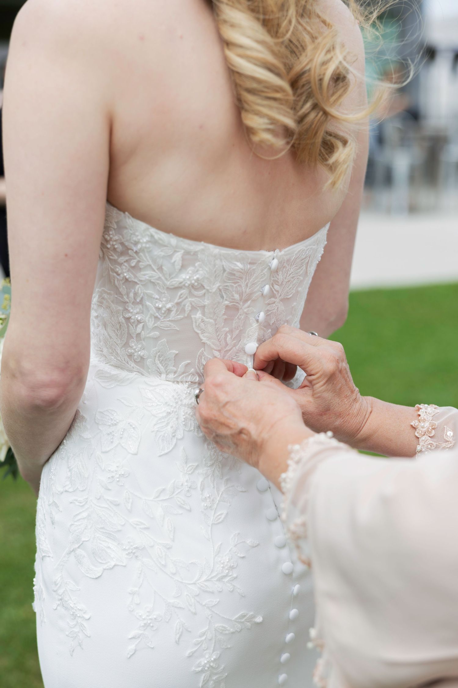 Close-up sequence showing the back of a white lace wedding dress being laced up and adjusted.