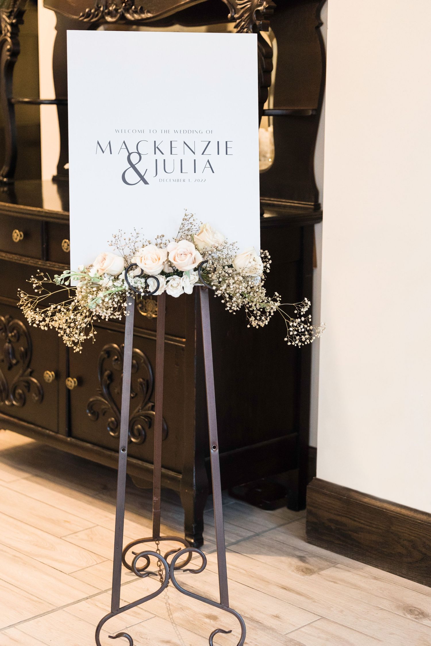 Elegant wedding welcome sign with floral decorations displayed on metal stand.