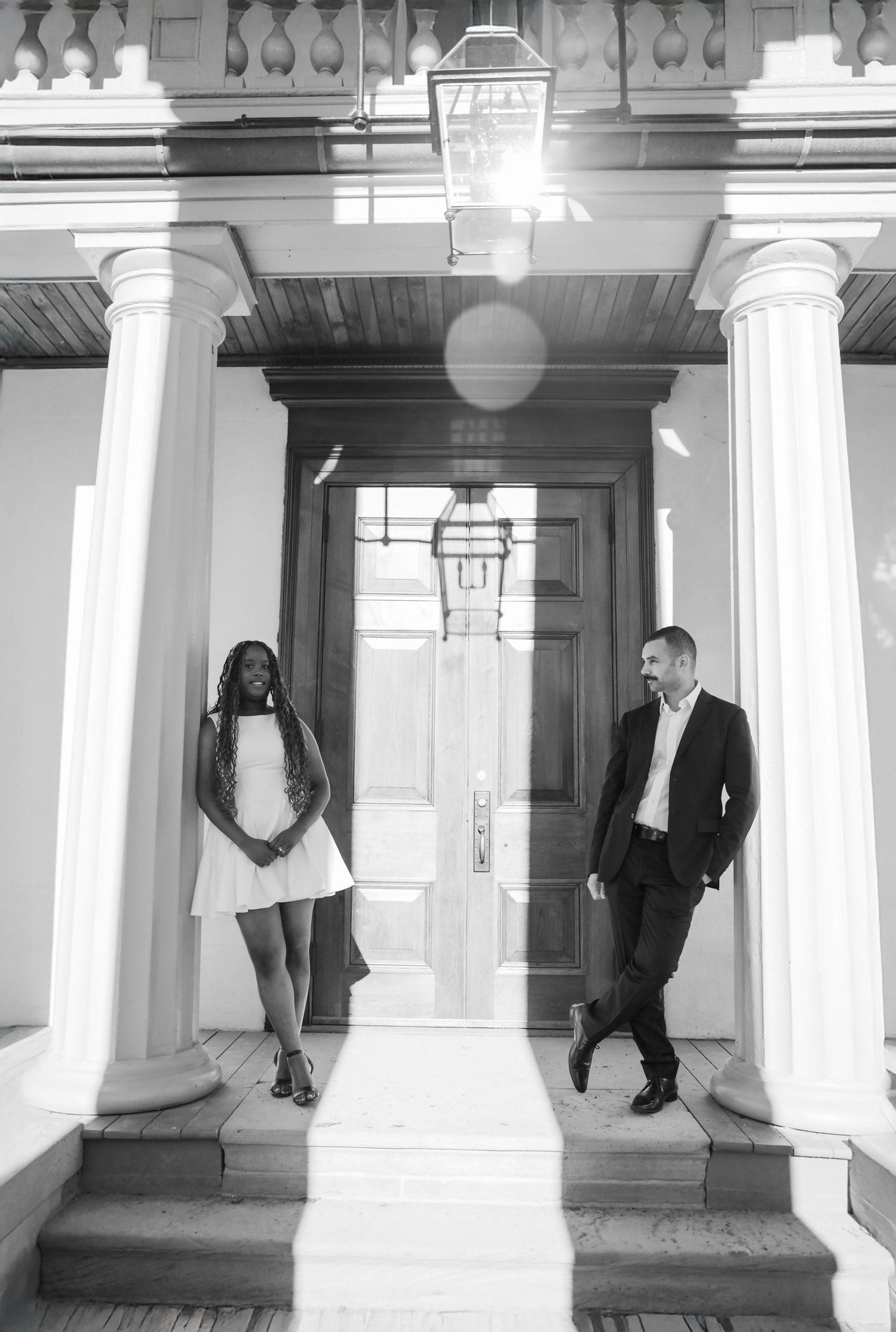 Black and white photo of a couple posing between columns at an elegant building entrance with a lantern above.