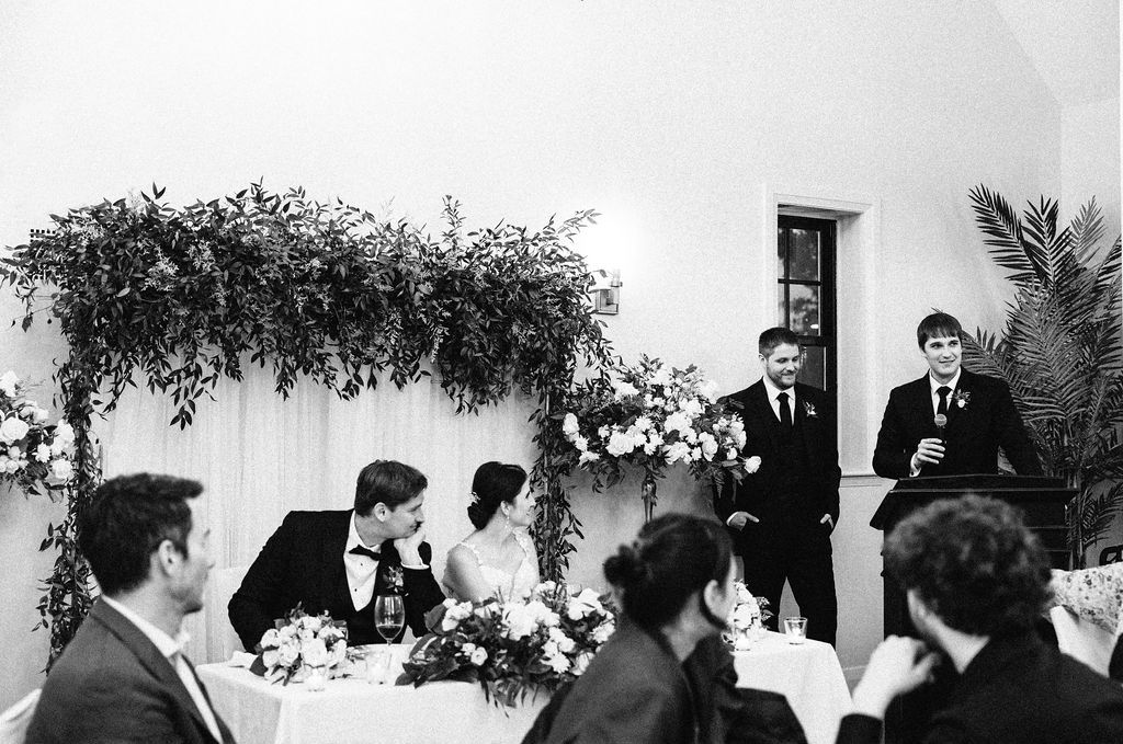 Black and white panoramic photo showing a formal wedding reception with guests seated at decorated tables.