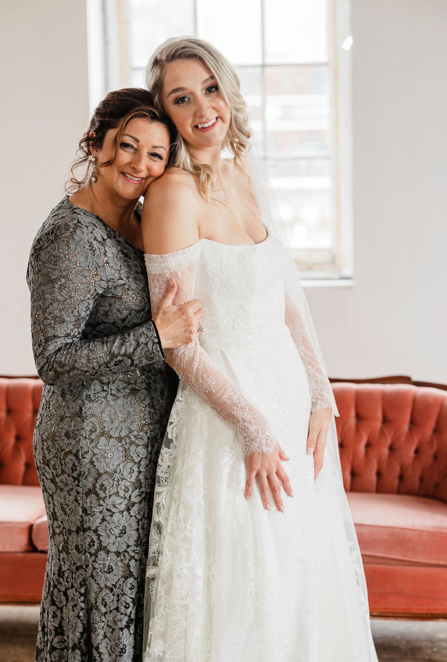 Joyful wedding portraits showing emotional embrace between bride and guest in grey lace dress.