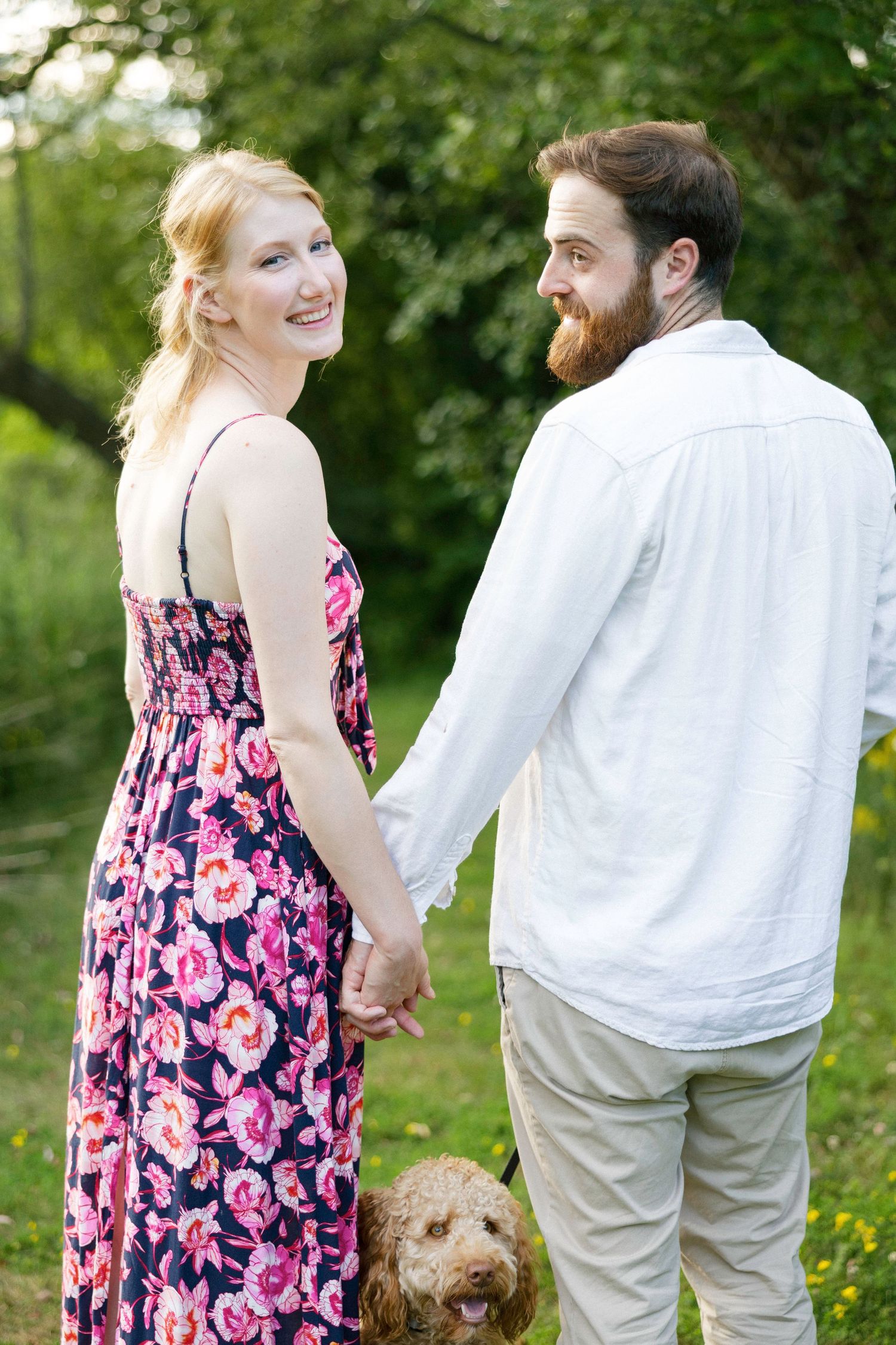 Couple holding hands in garden with their goldendoodle dog.