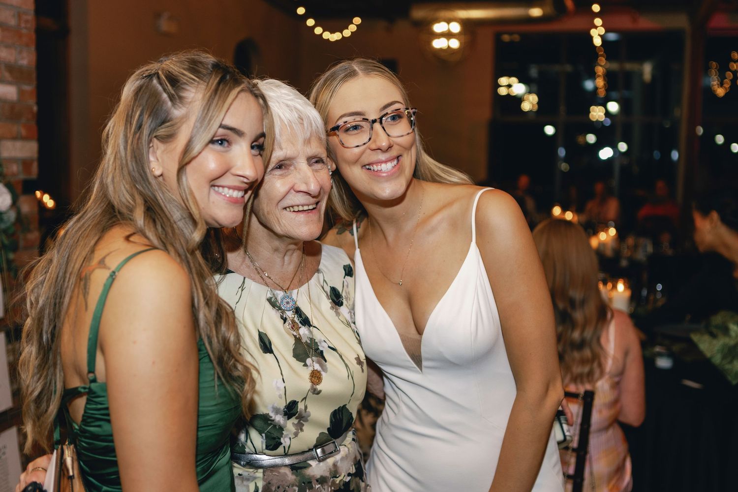Party guests socializing and smiling at an evening event with brick wall background.
