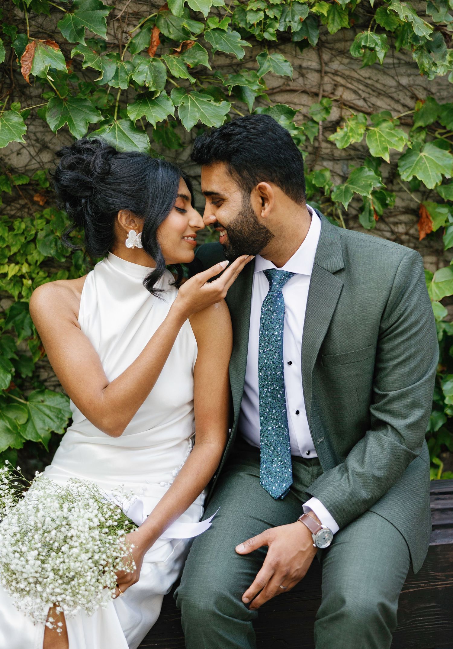 A romantic wedding couple shares intimate moments against a lush green ivy wall backdrop.