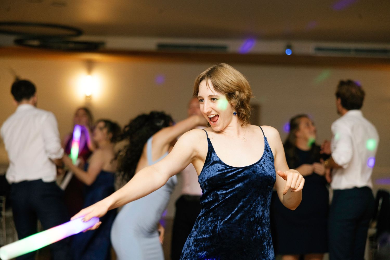 People dancing and celebrating at a wedding reception with colorful lights and decorations in a banquet hall.