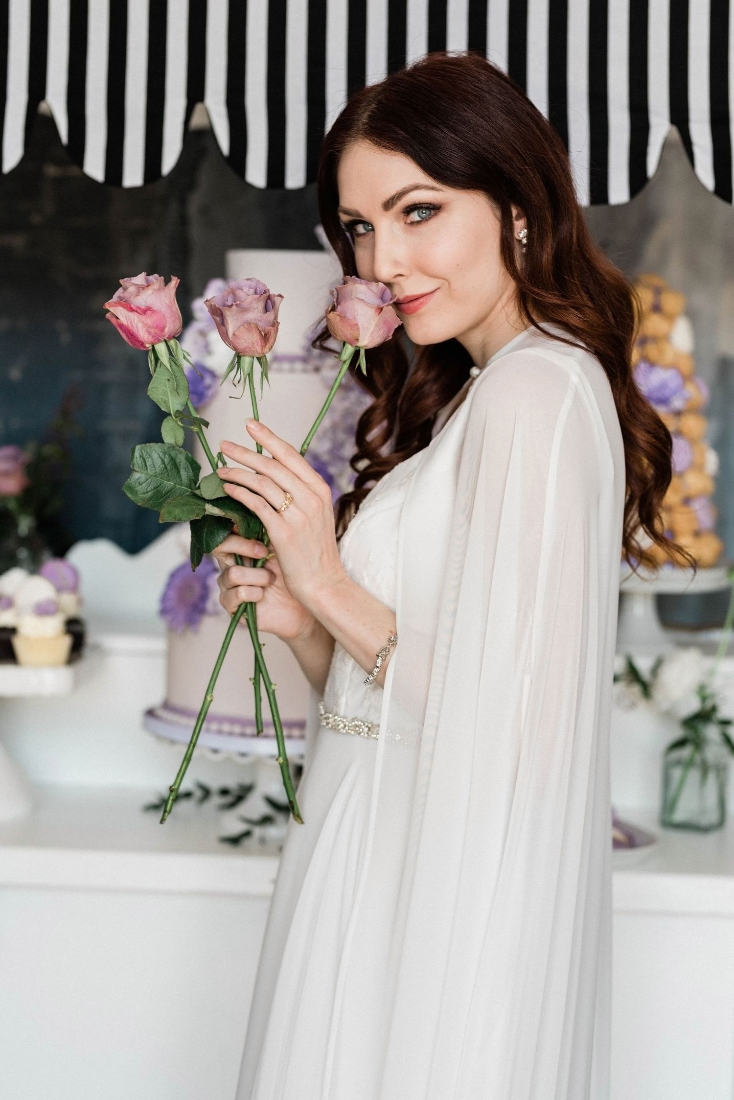 Elegant figure in white robe holding delicate pink roses against dark background.