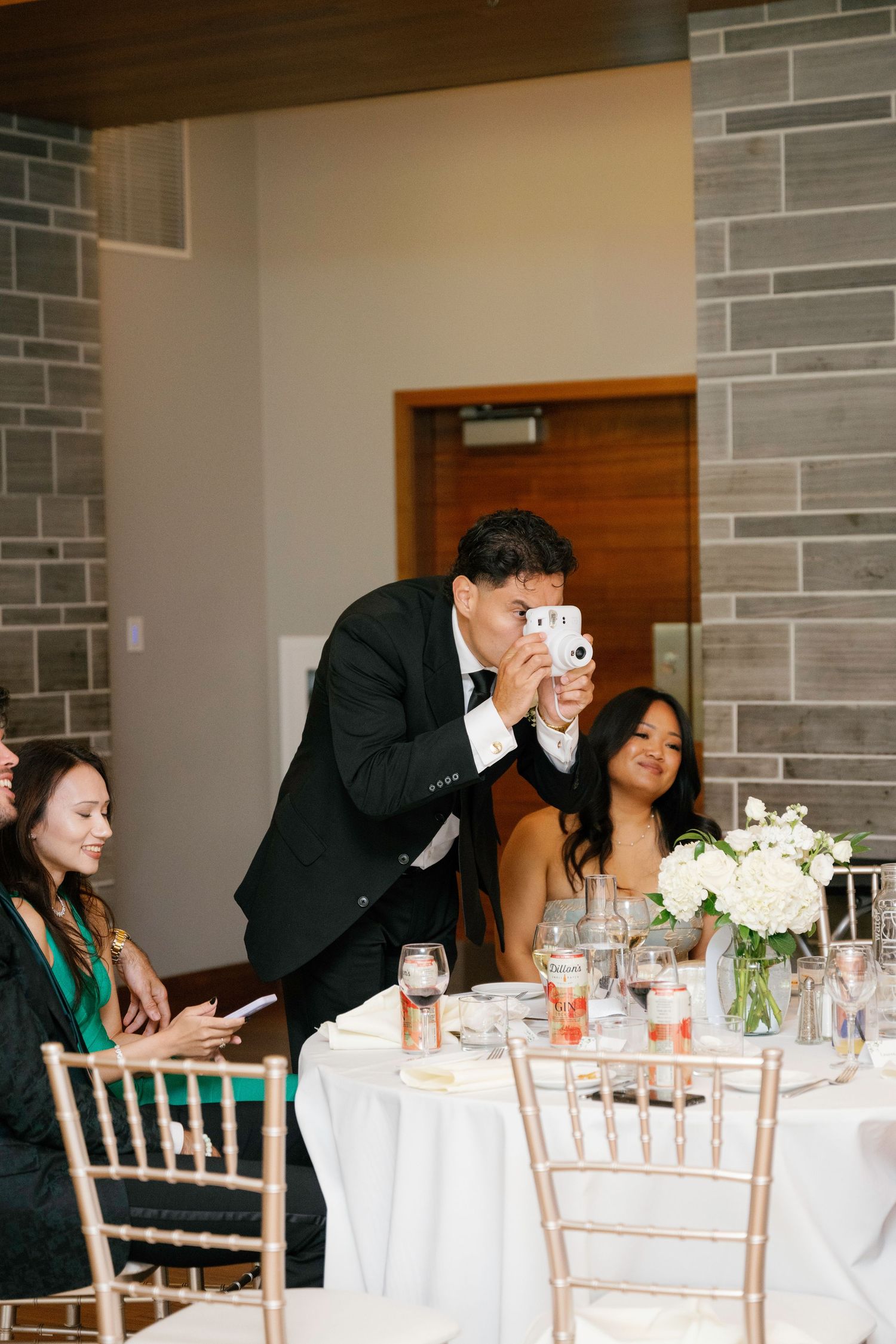 Wedding guests share laughter and conversation at an elegant reception table with white floral centerpieces.