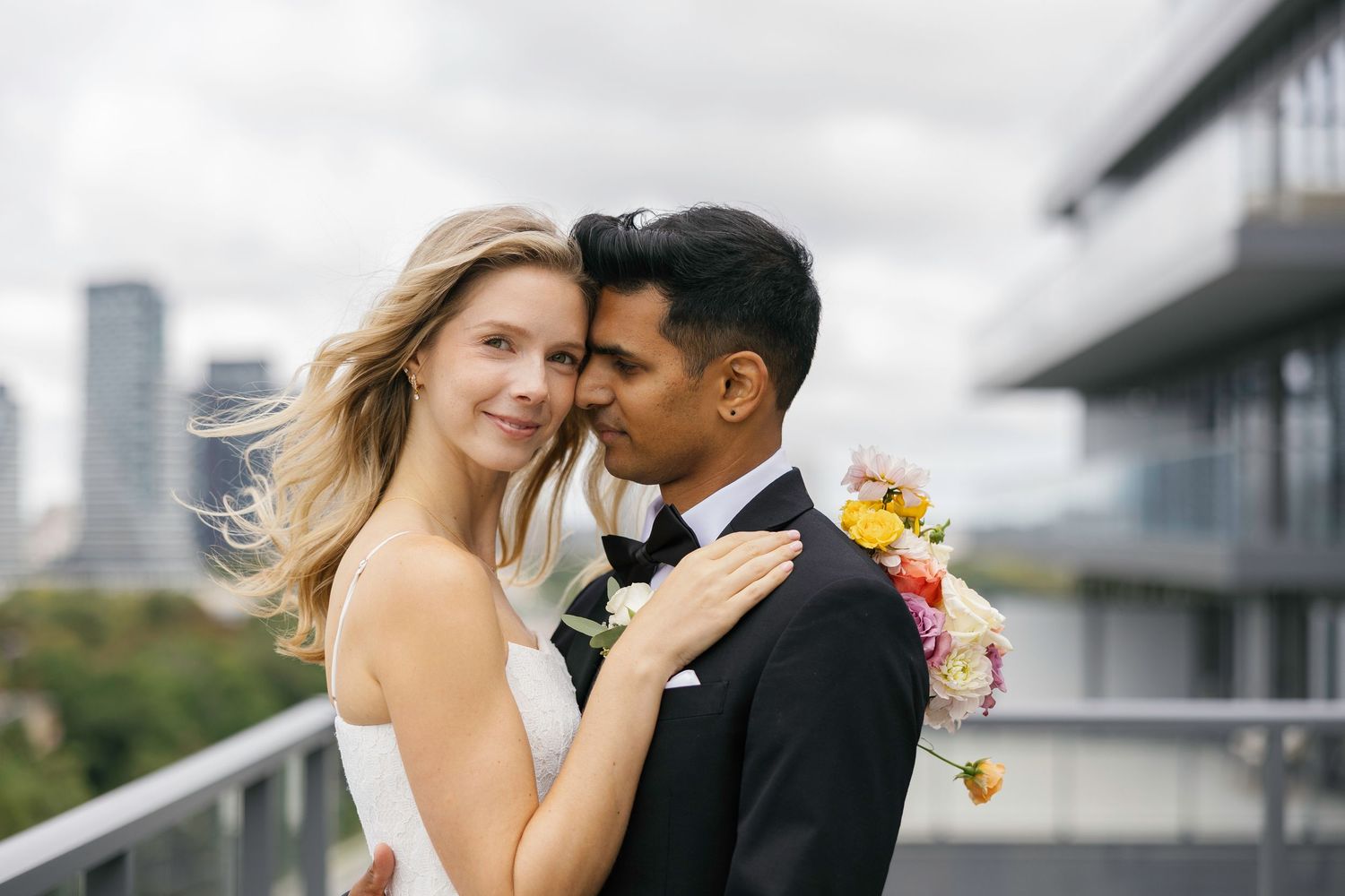 Bride and groom sharing a romantic moment on a rooftop with city skyline backdrop on their wedding day.