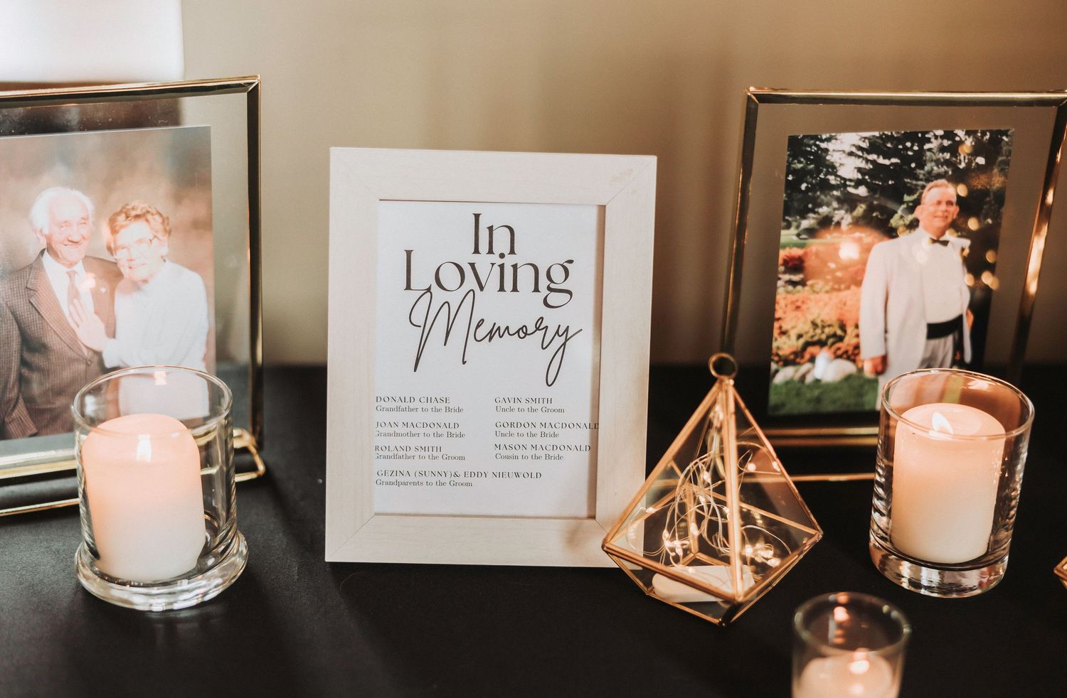 Elegant wedding memorial table with glowing candles and geometric gold frames displaying sentimental messages.