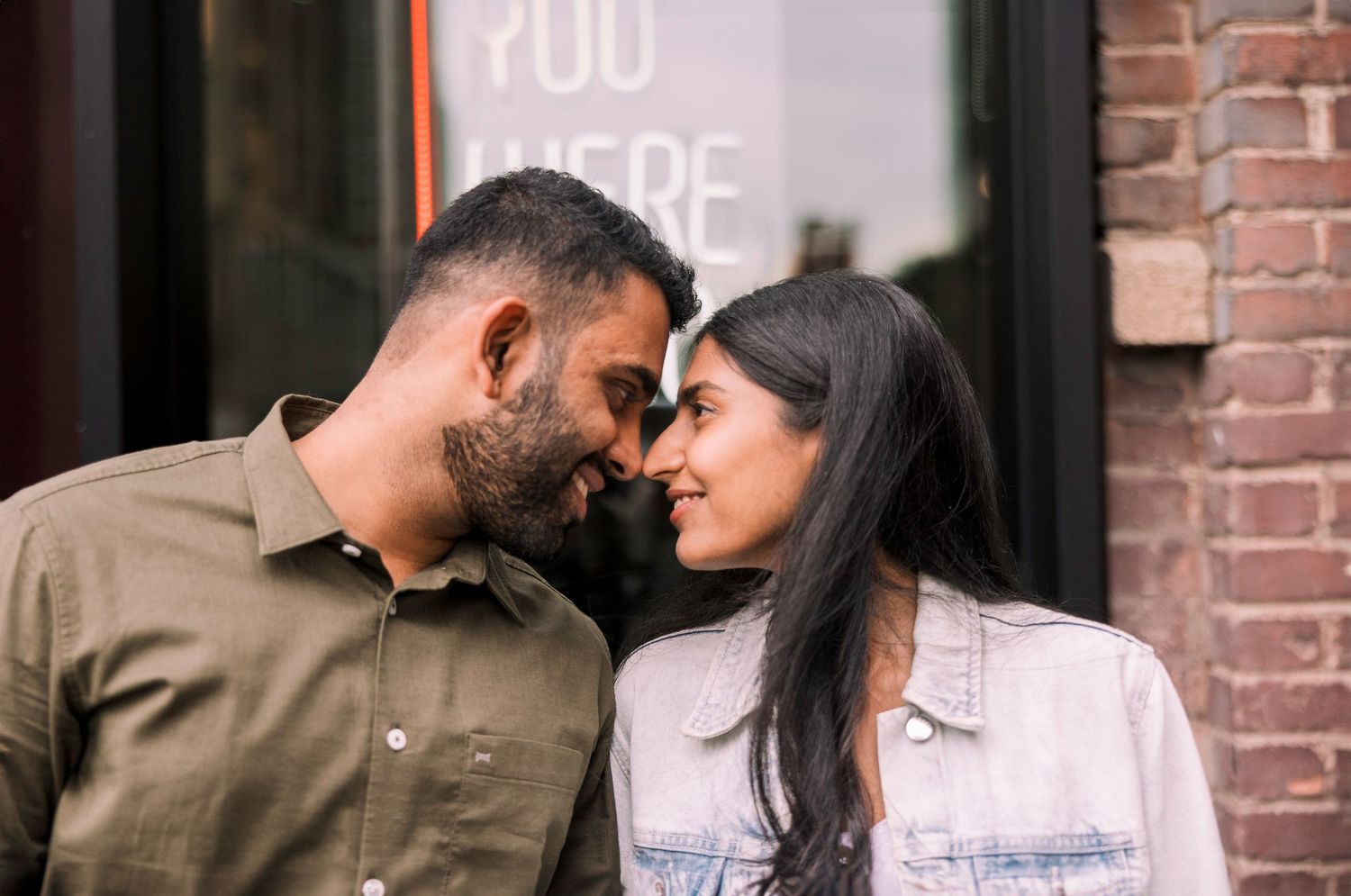 Romantic couple sharing intimate moment against brick wall background.