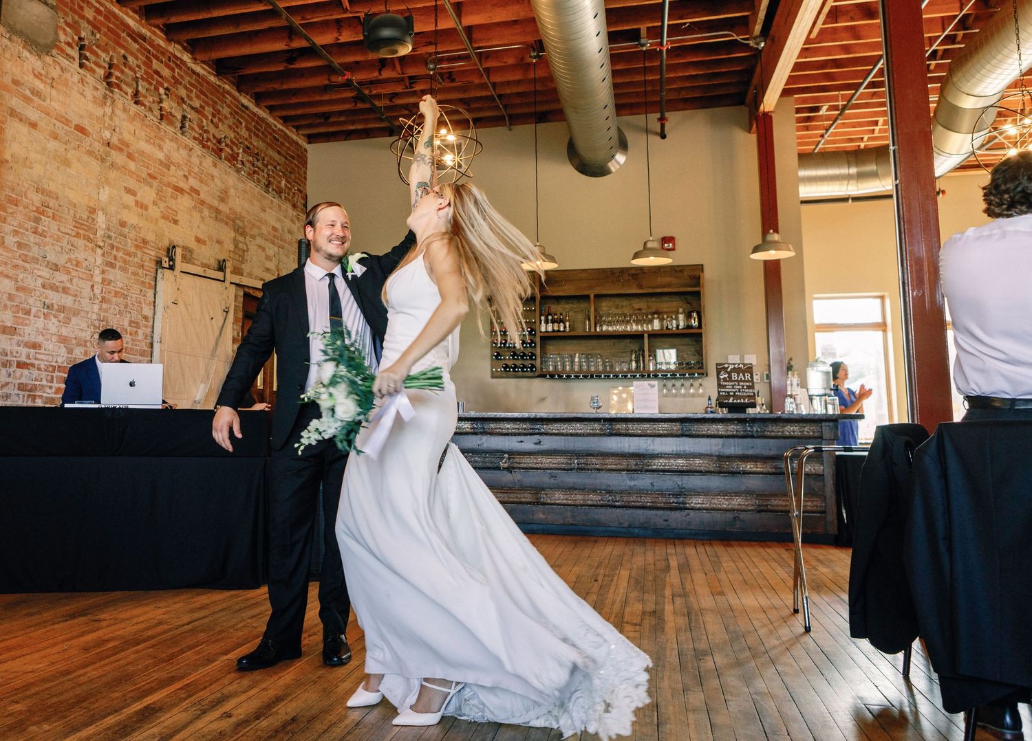 A couple dances in an industrial-style venue with exposed brick walls and wooden floors during their wedding celebration.