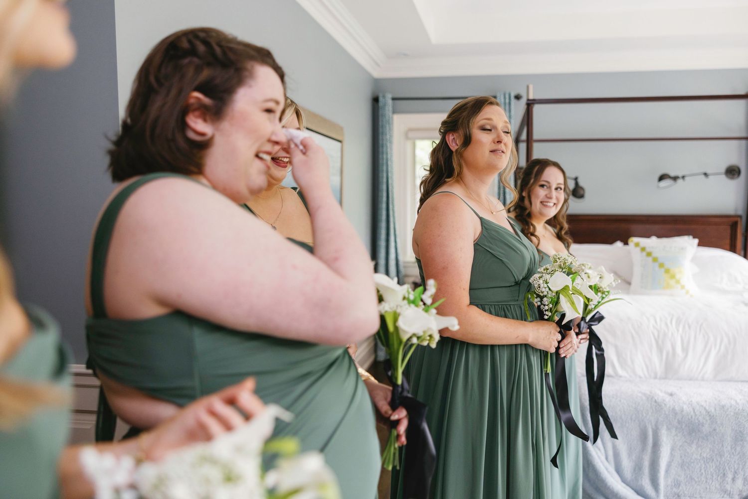 Bridesmaids in sage green dresses share laughs during pre-ceremony preparations.