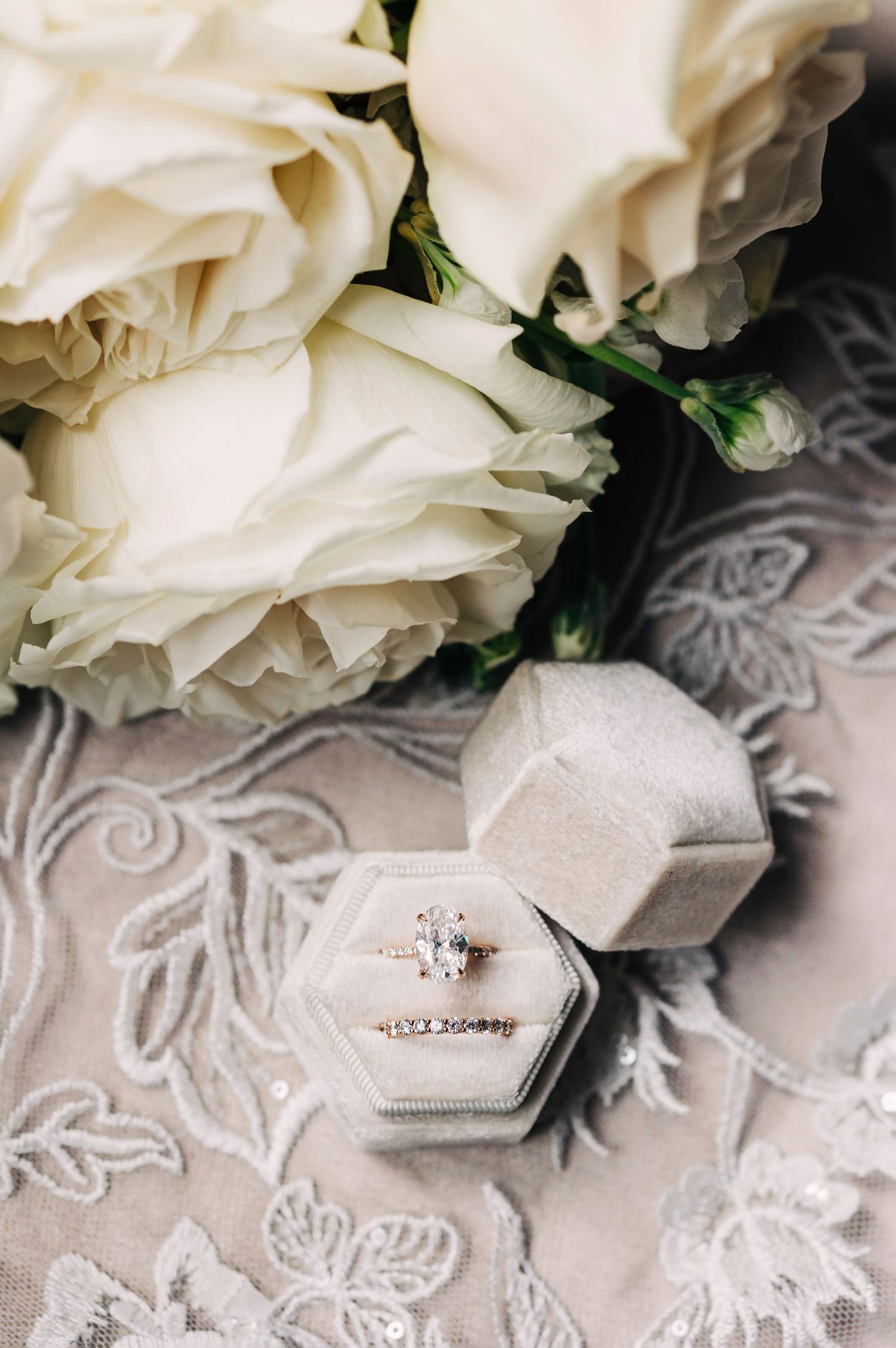 White roses and engagement ring box displayed on lace textured fabric.