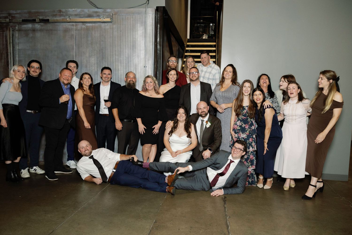 Large group of elegantly dressed people posing together at a wedding reception in an industrial venue.