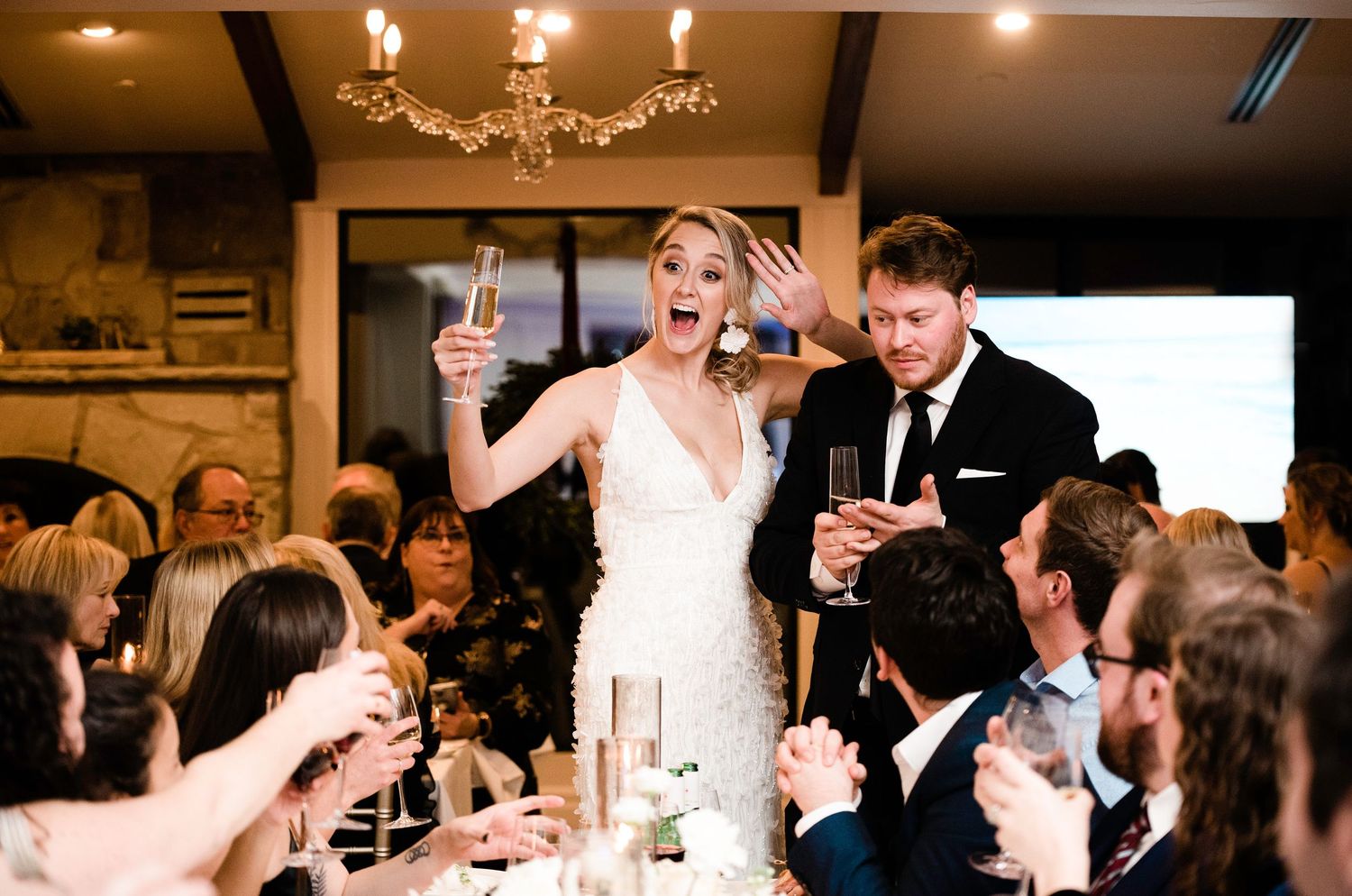 Bride and groom toast champagne with guests during lively wedding reception celebration.