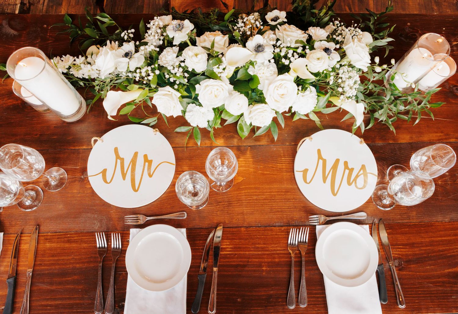 White floral arrangements and decorative signage adorn a rustic wooden beam at an elegant wedding reception venue.