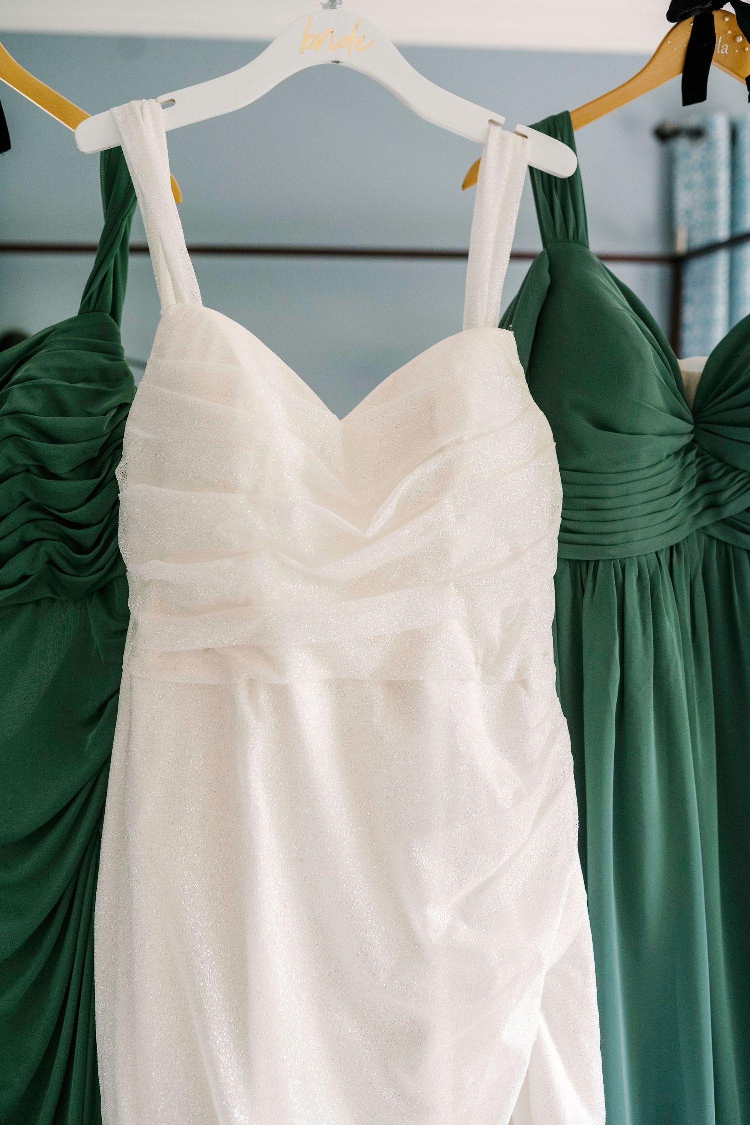 White wedding gown hangs alongside sage green bridesmaid dresses on display.