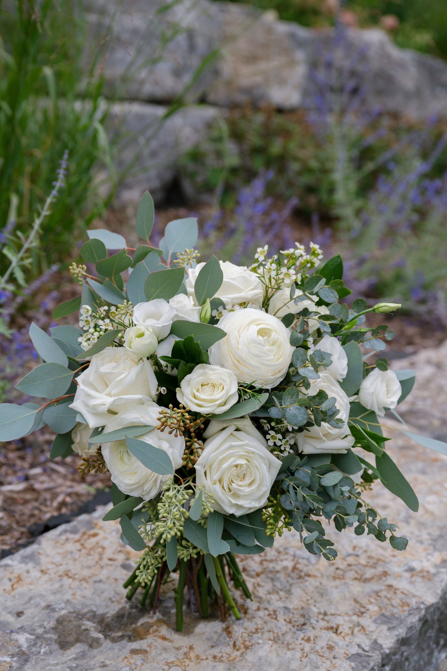 A romantic white rose and eucalyptus wedding bouquet photographed from different angles on a stone surface outdoors.