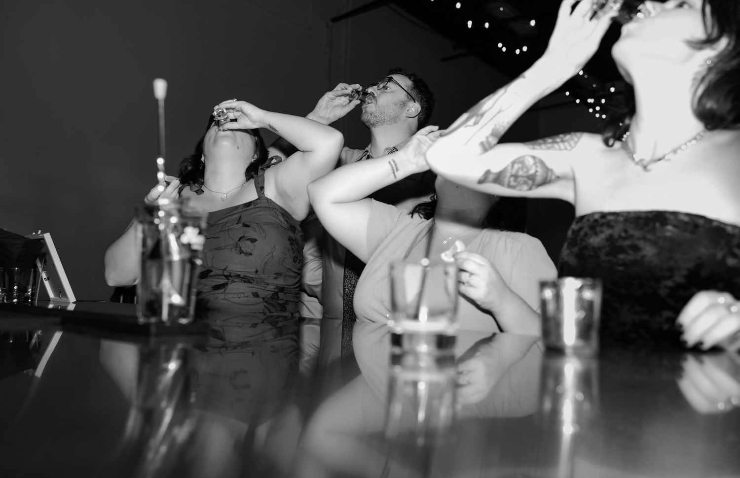 Black and white photo of women taking shots at a bar, laughing and celebrating together.