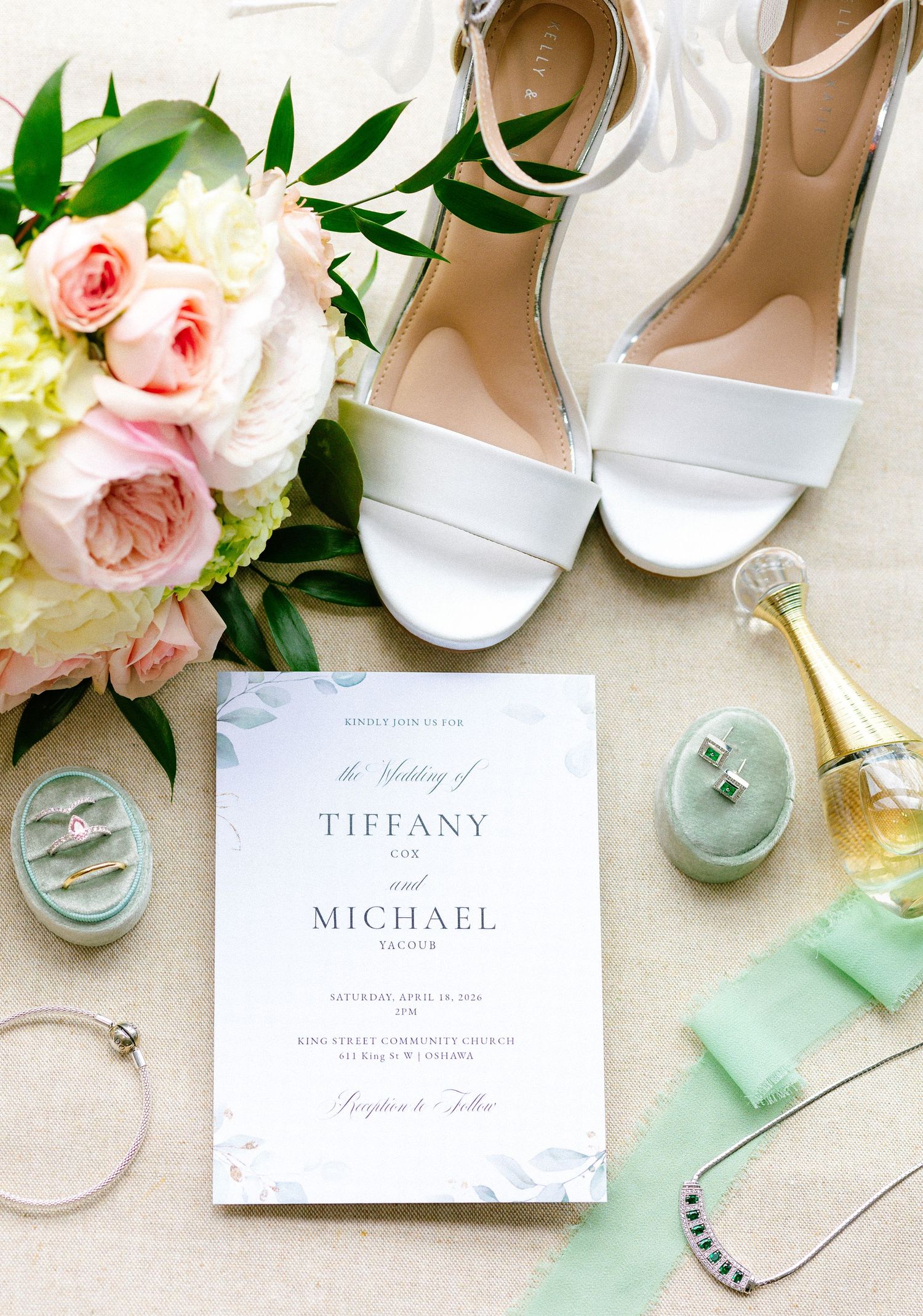 Elegant wedding flat lay with white heels, floral bouquet, invitation for Tiffany and Michael, jewelry, and perfume on neutral background.