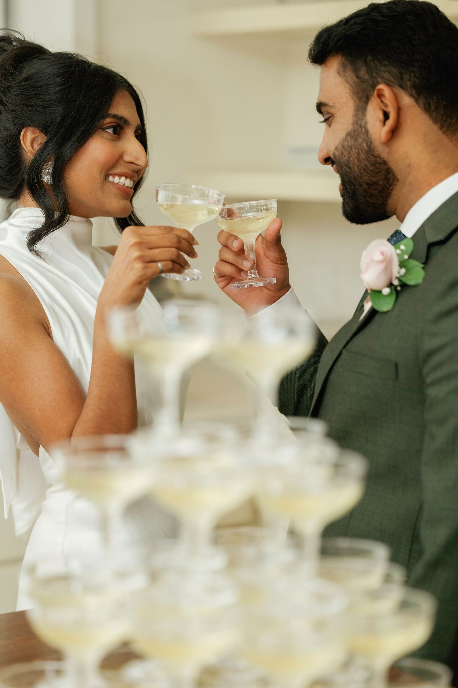 Couple toasting champagne glasses at wedding reception with champagne tower in foreground.