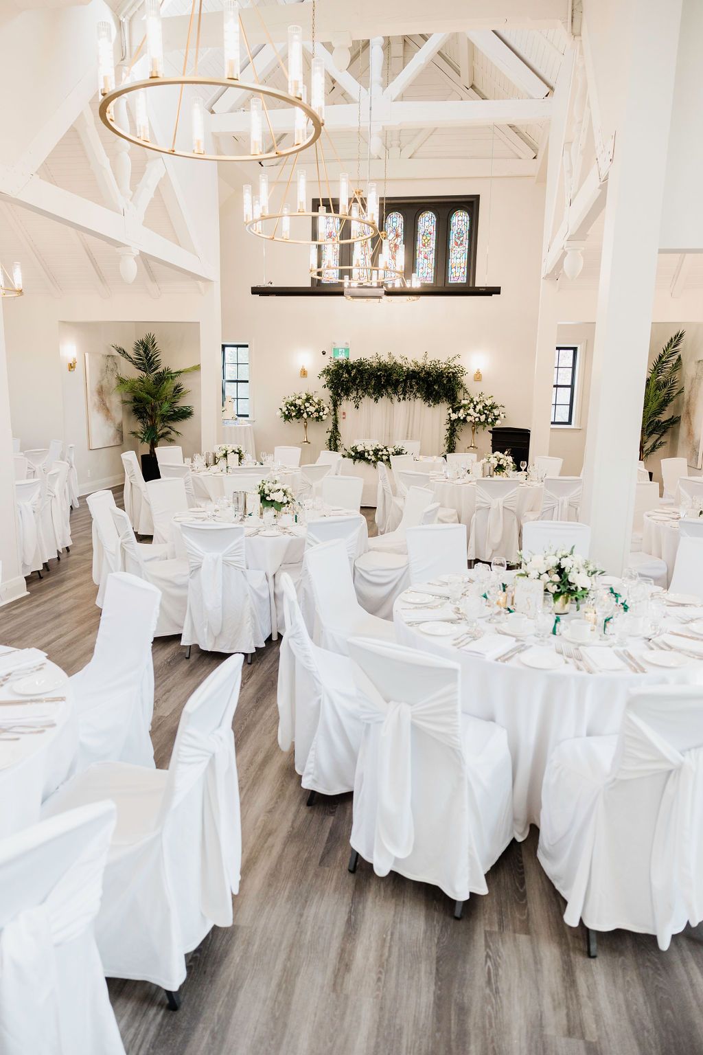 White reception hall with round tables, chair covers, and rustic wooden beams.