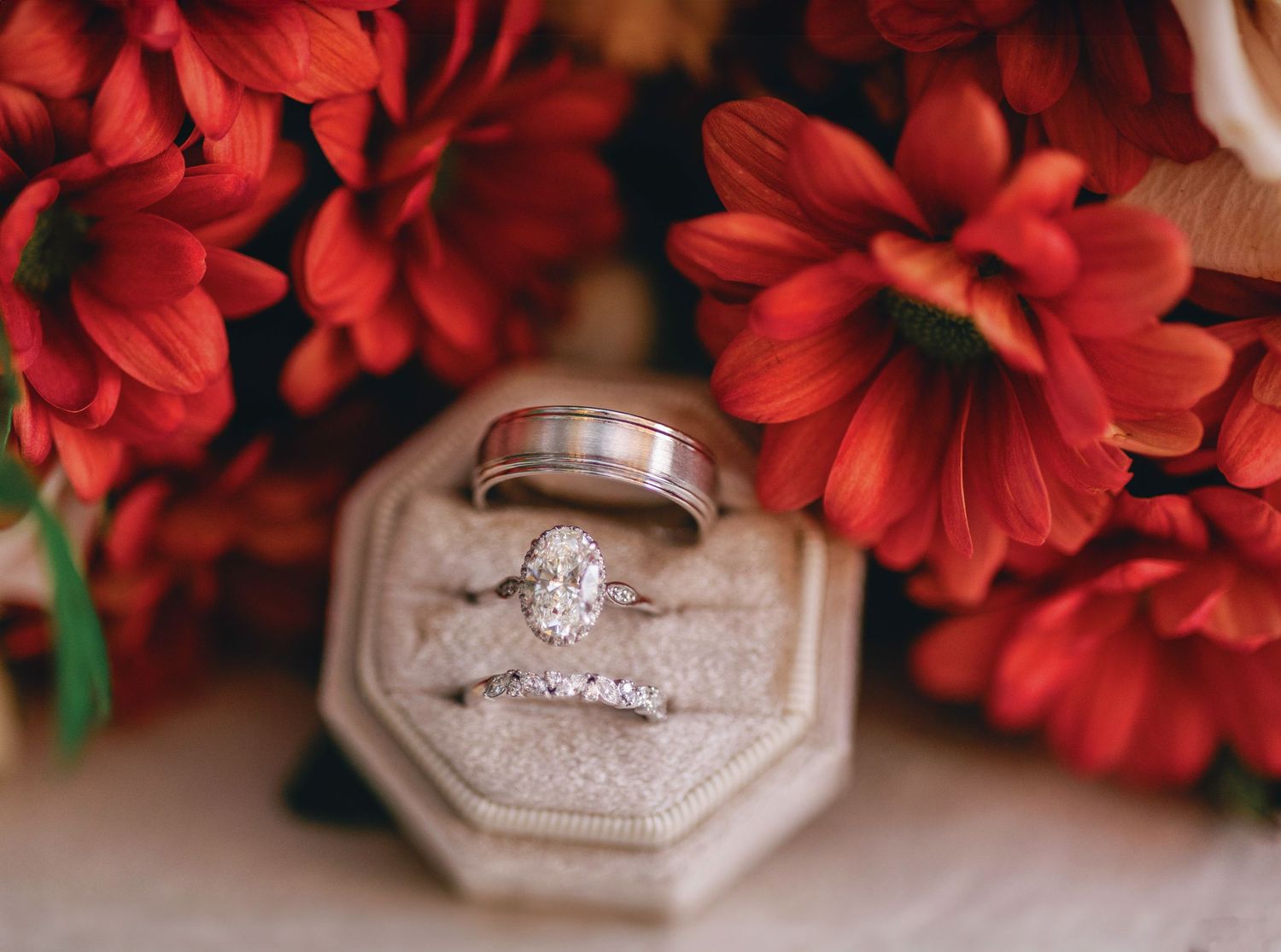 Wedding rings displayed in hexagonal box with vibrant red flowers in background.