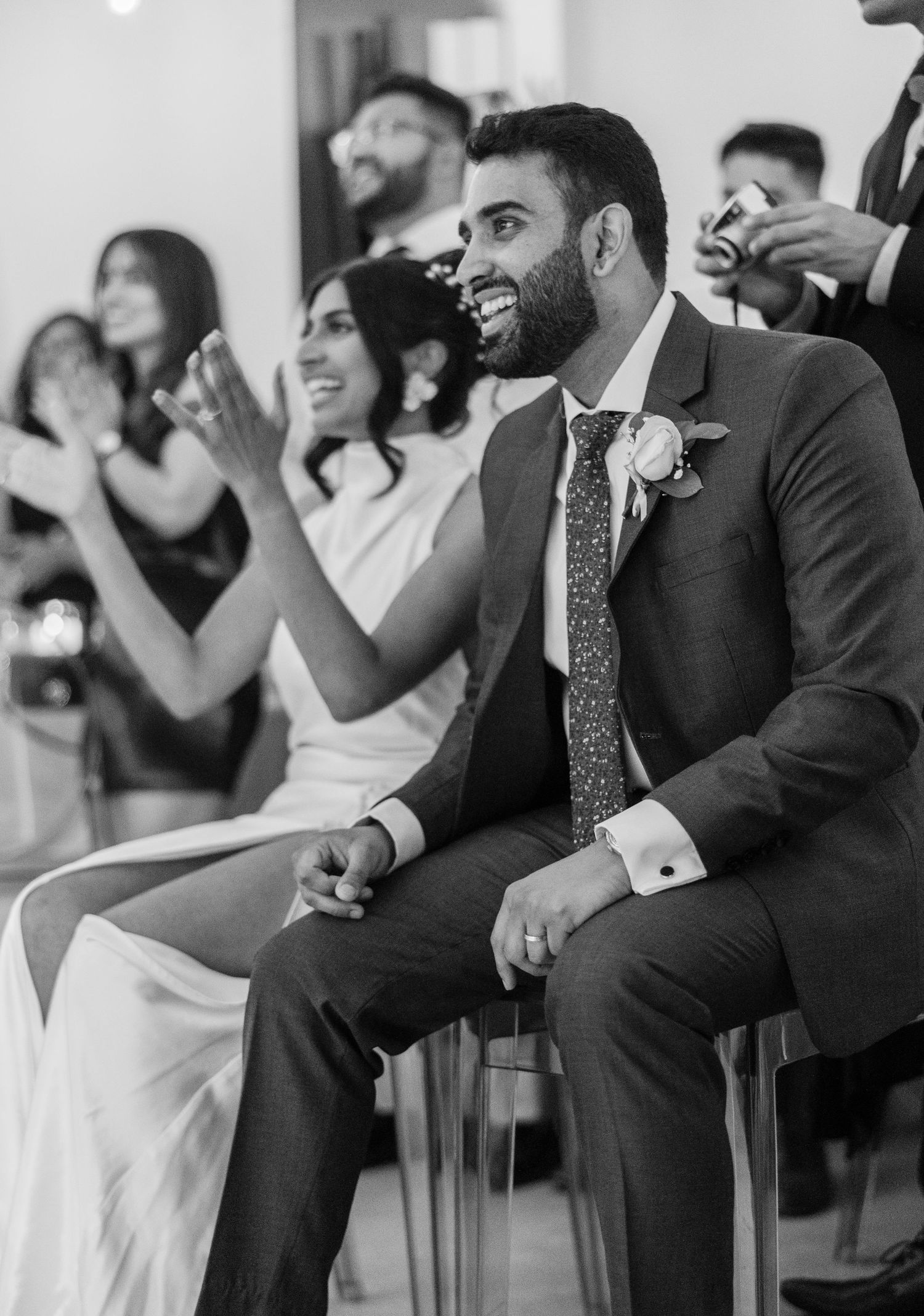 Wedding guests and couple laughing during reception speeches in black and white.