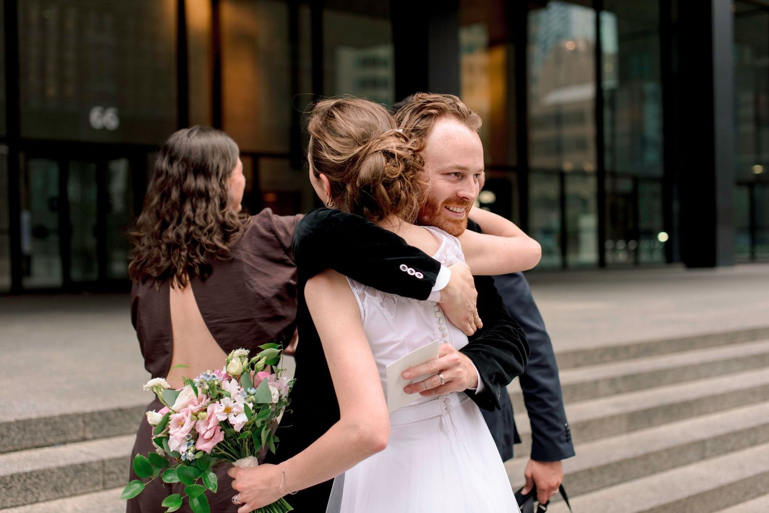 Guests sharing emotional embraces outside a modern building.