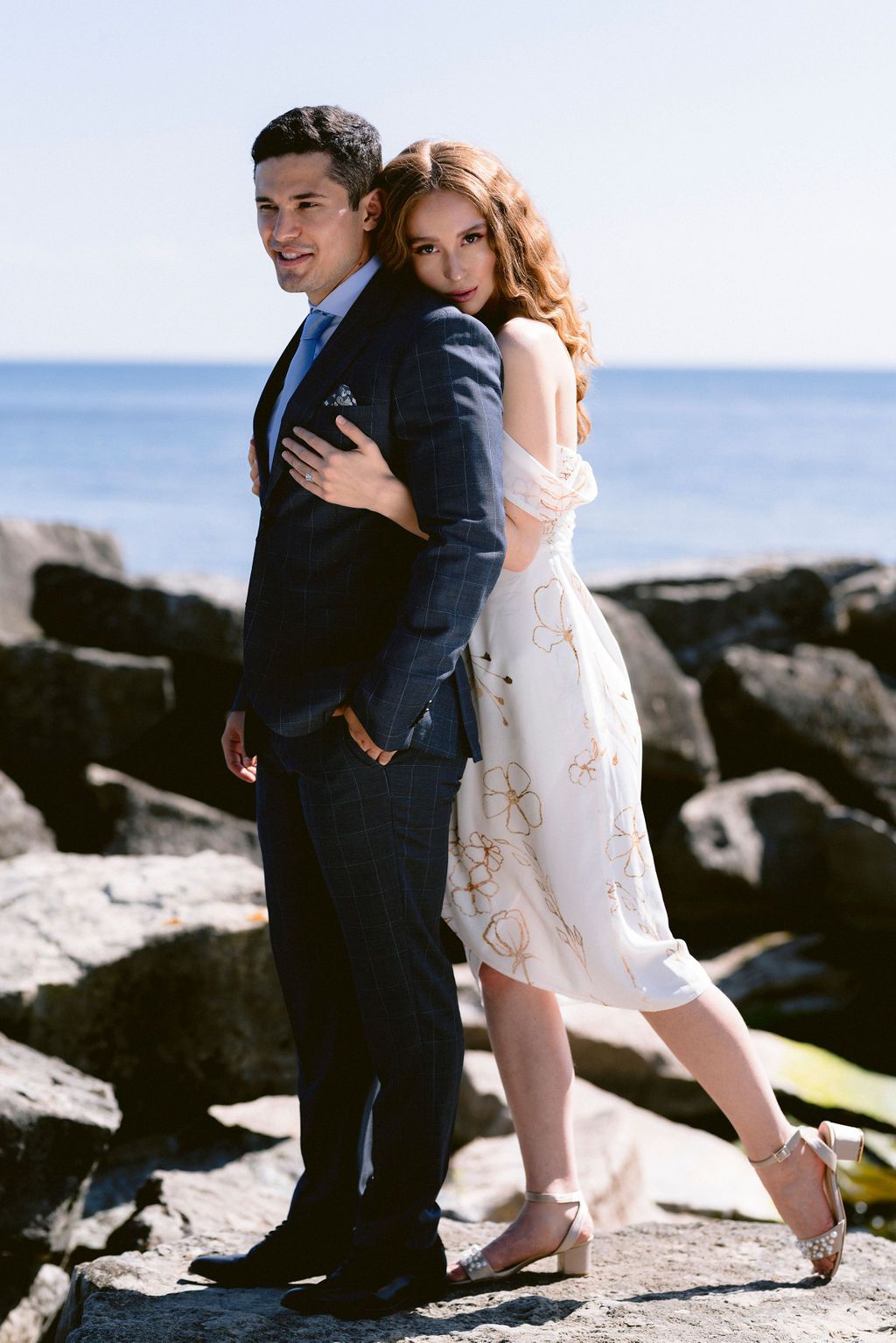 Romantic coastal wedding photos on rocky beach with couple in formal attire.