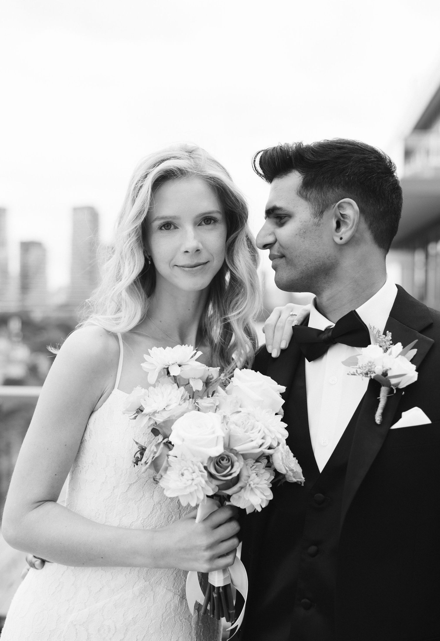 Black and white wedding portrait of a blonde bride holding a bouquet and groom in a tuxedo with boutonniere.