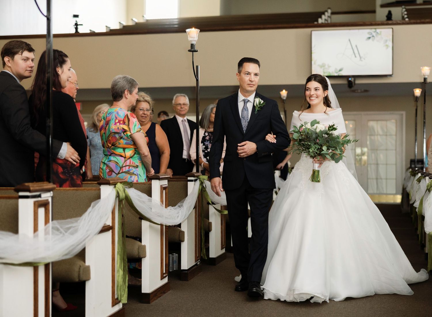 Bride and groom walk down the aisle at a church wedding ceremony, bride holding white floral bouquet.
