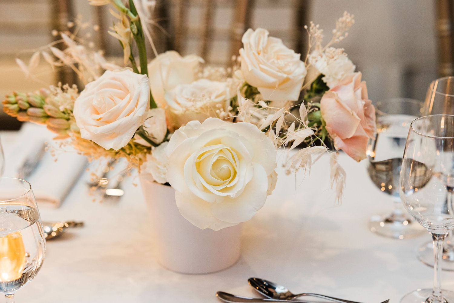 Elegant floral centerpieces with white and blush roses decorate wedding reception tables.
