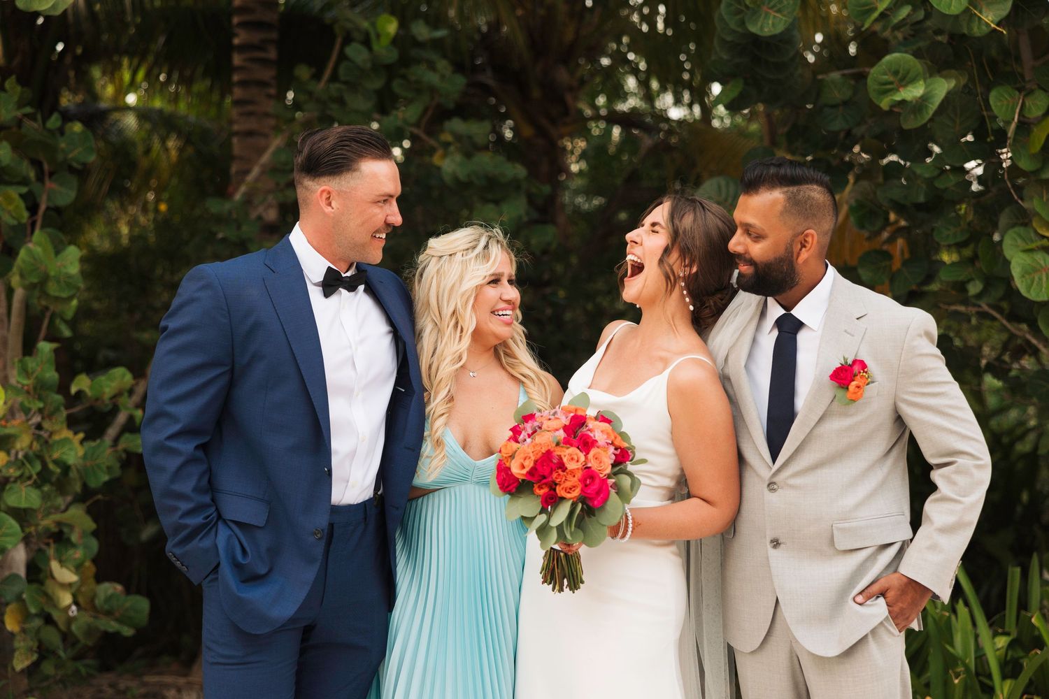 Wedding party in navy and mint green attire pose together in a garden setting with coral bouquets.