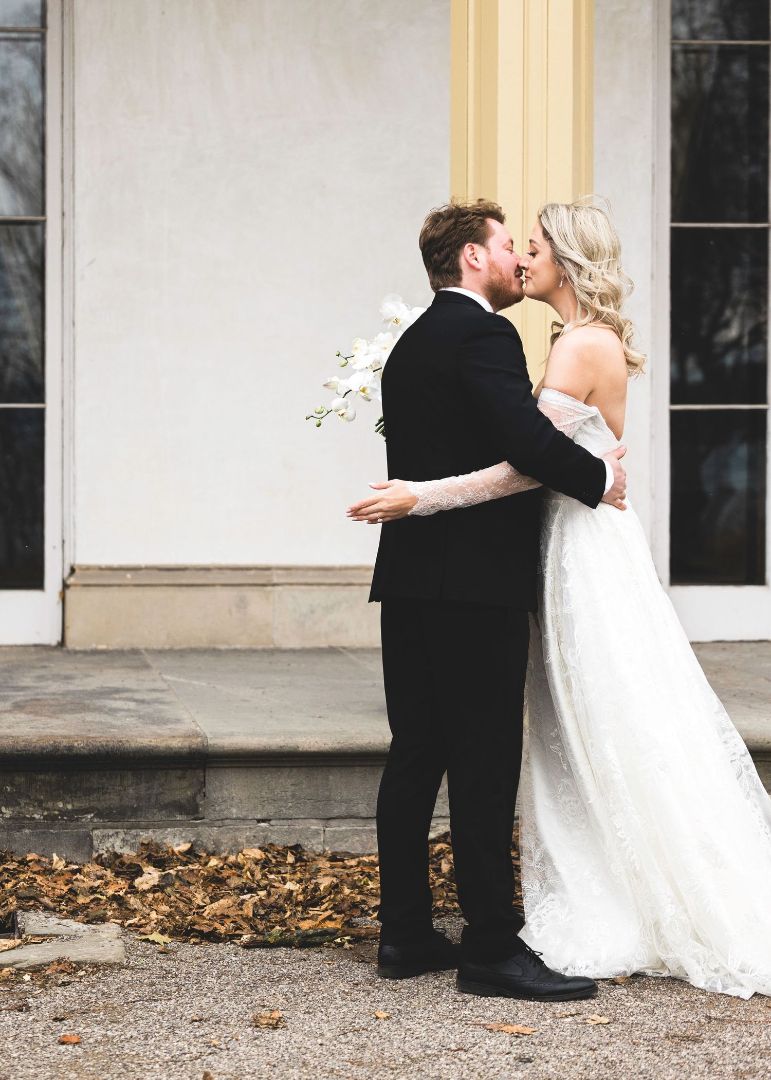 First look wedding moment captured outside historic building with autumn leaves.