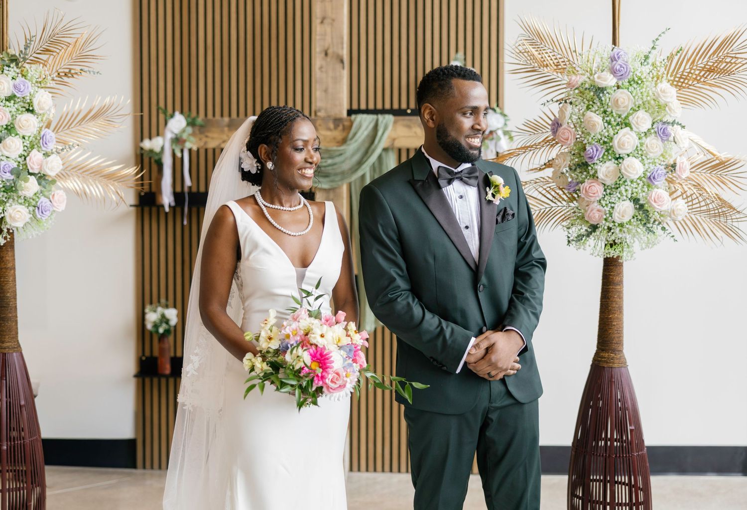 A bride and groom stand at the altar during their wedding ceremony, surrounded by tropical floral arrangements.