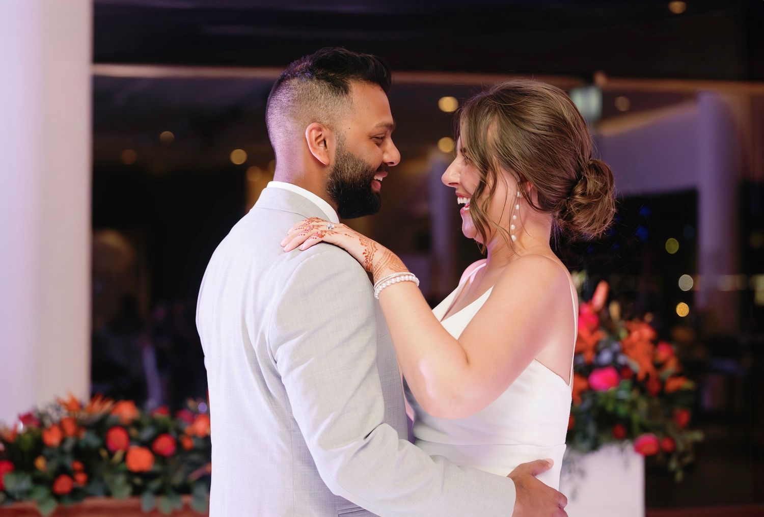 A couple shares a romantic dance together during their wedding reception with soft lighting and floral decorations.