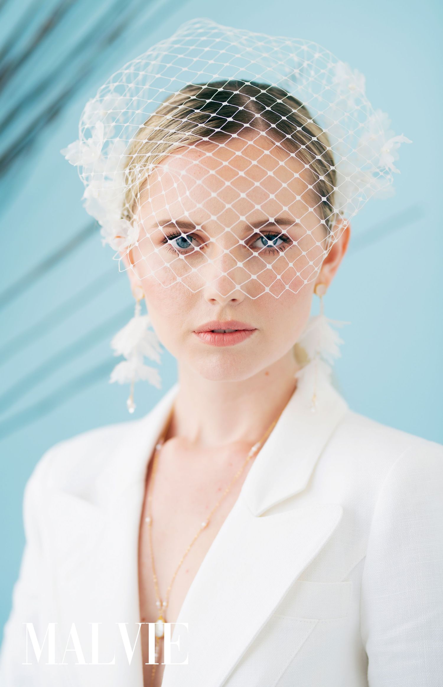 Bridal portraits with vintage-style white birdcage veil against light blue backdrop.