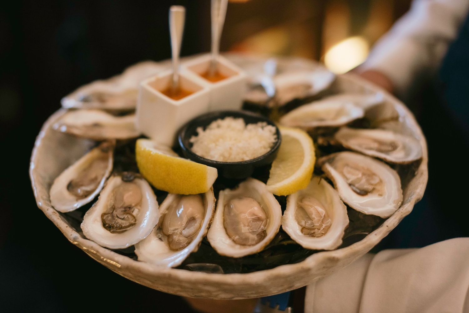 Fresh oysters arranged on ice with lemon wedges on a white serving platter.