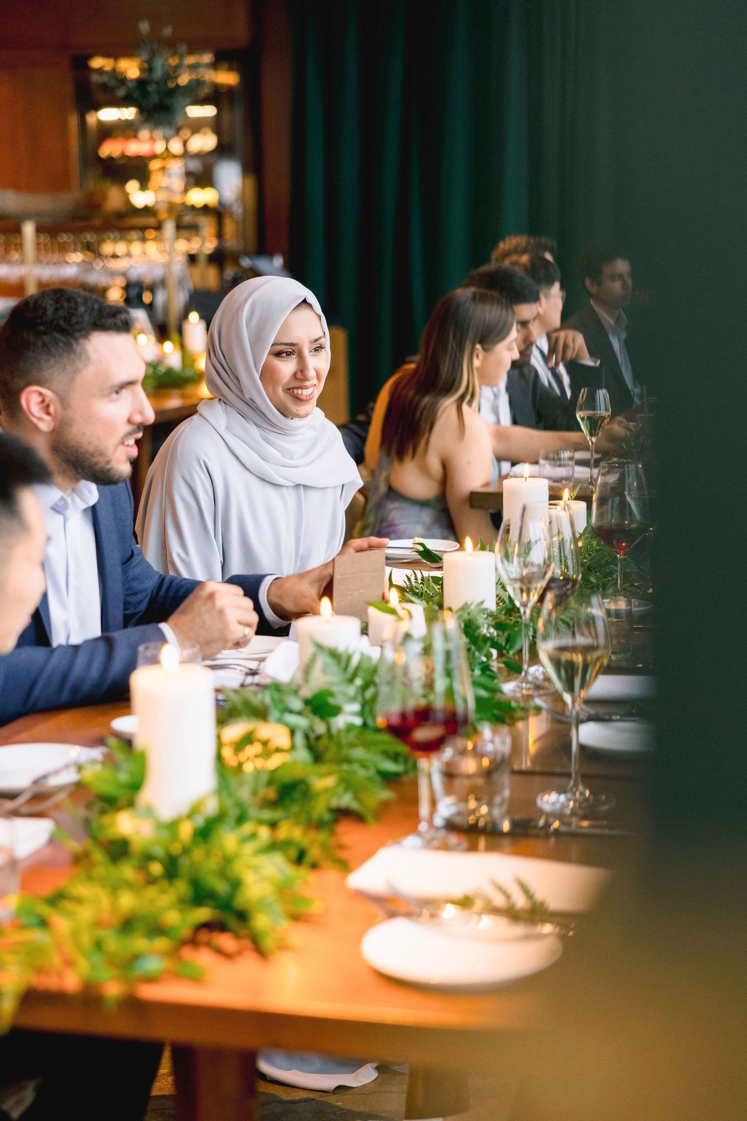Guests enjoying a formal dinner at an upscale restaurant with elegant table settings and greenery centerpieces.