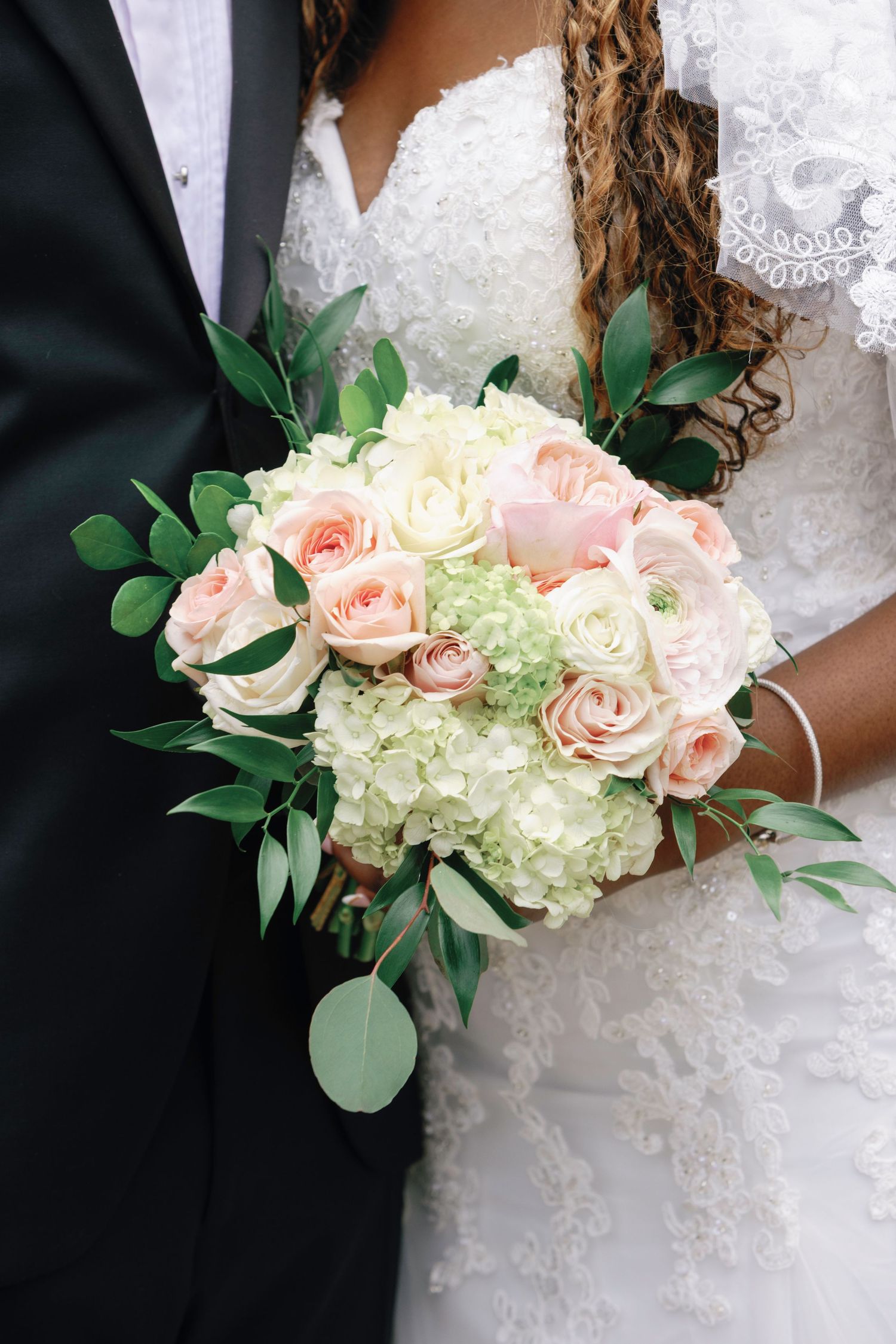 Bride and groom holding a elegant wedding bouquet of blush pink roses and white hydrangeas with greenery.