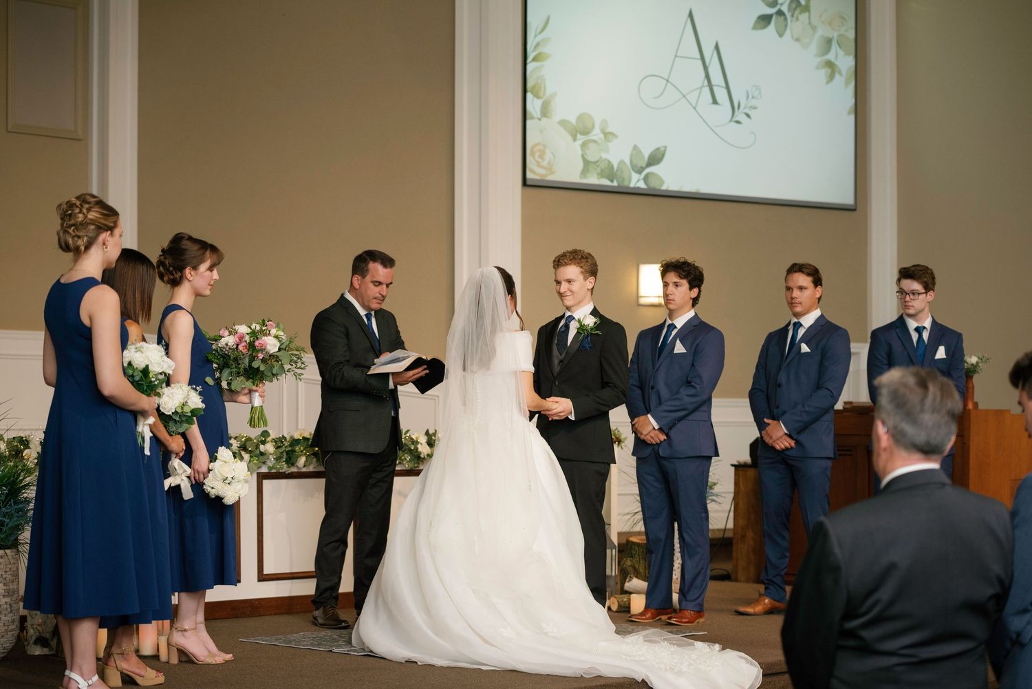 Bride and groom exchange vows at elegant church wedding ceremony with bridesmaids in navy blue dresses and groomsmen.