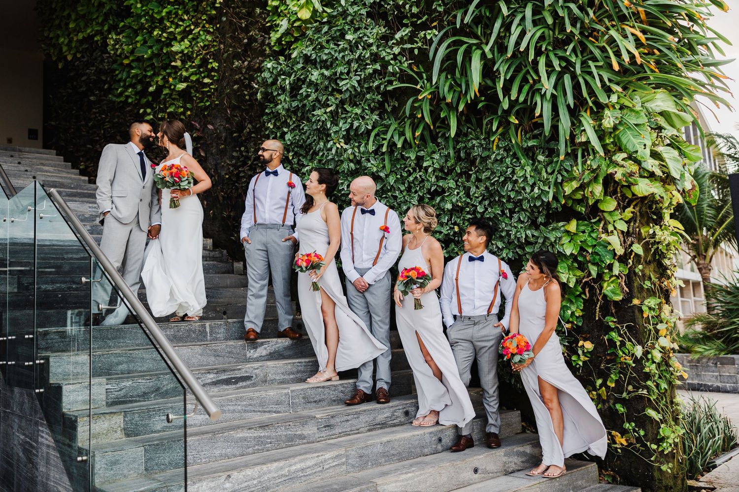 Wedding party in gray attire poses on steps before a lush green living wall backdrop.